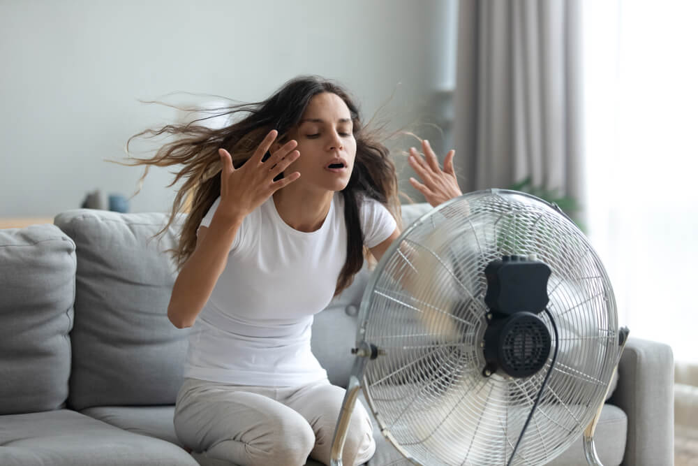 Tired woman in overheated room during UK heatwave highlighting need for portable air conditioning over basic fans