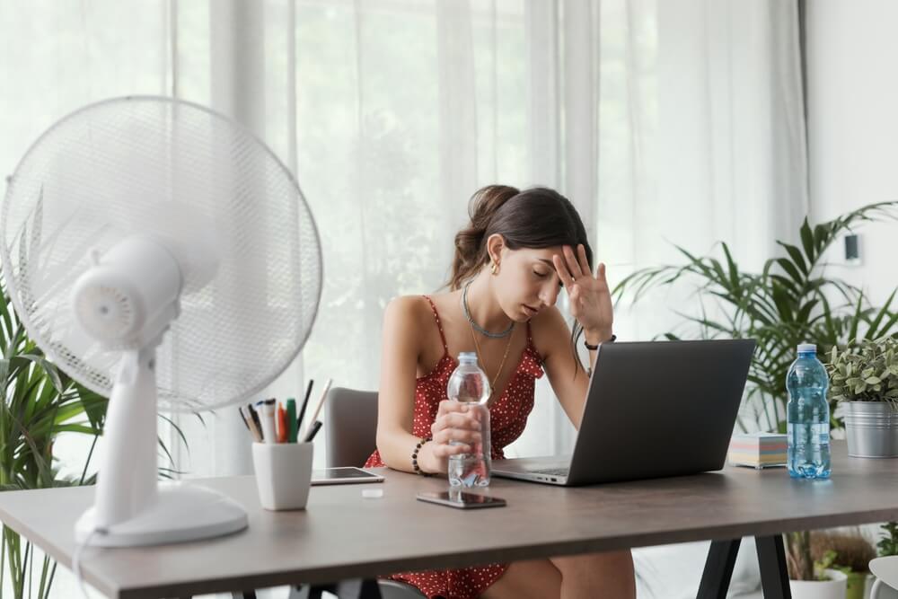 Woman overheating while working indoors during summer, illustrating need for temporary air conditioning in UK offices
